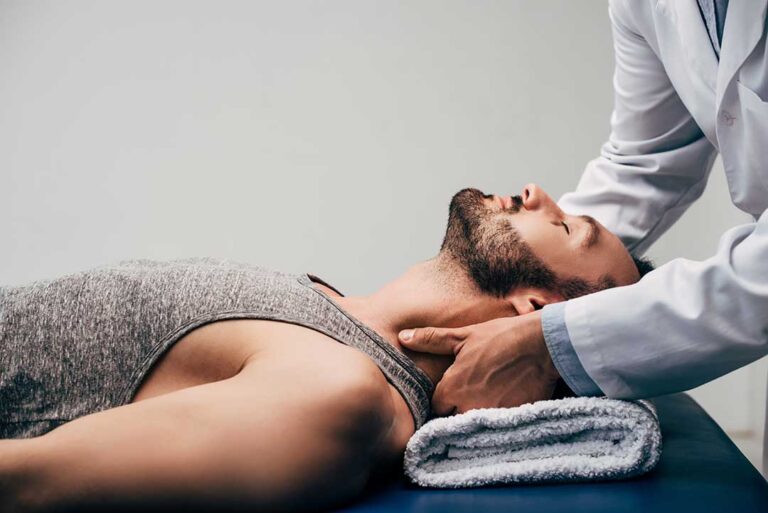 A chiropractor gently checking a patient's lower back while discussing health concerns in a treatment room.