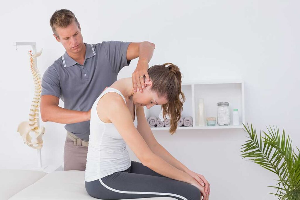 Adult receiving a gentle back adjustment while lying face down in a bright clinical room.