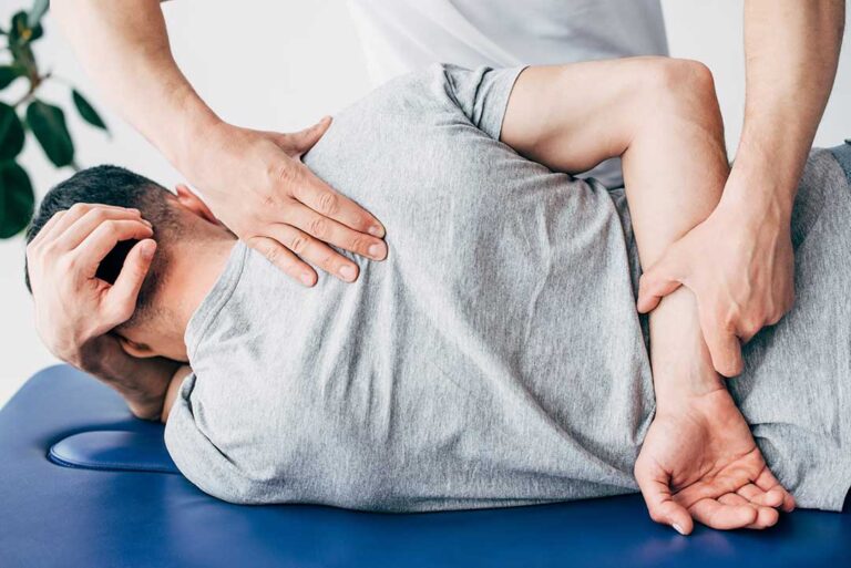 An adult bending their knees to lift a box with a straight back in a home garage setting.